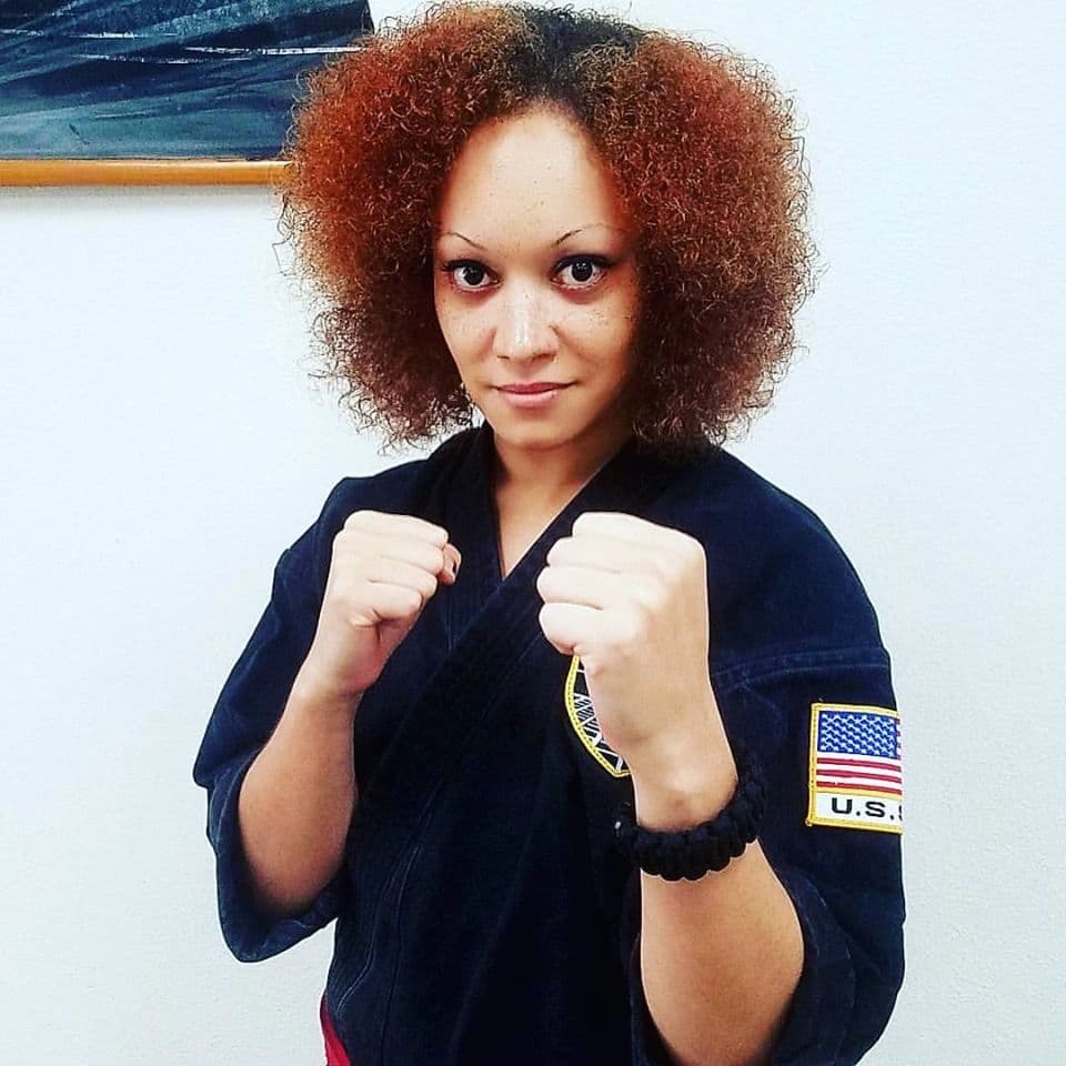 Woman in martial arts uniform with fists raised, ready to fight.